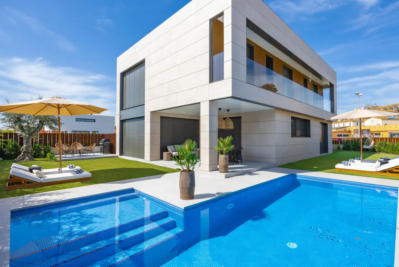 Vivienda unifamiliar de dos plantas con fachada de piezas claras de gran formato, junto a una piscina.