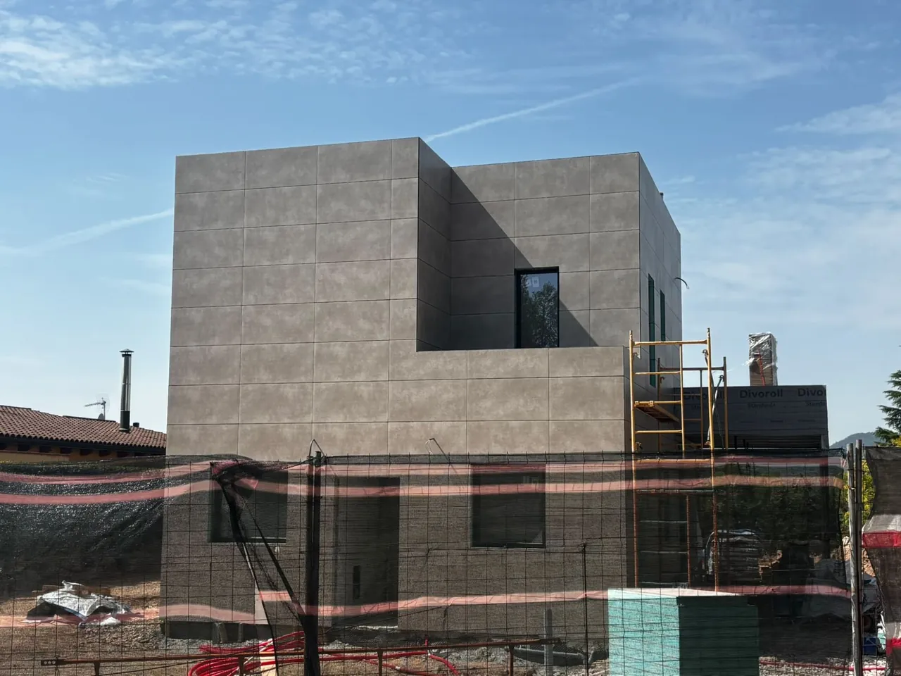 Vivienda de volúmenes cúbicos con fachada de piezas grises de gran formato, en la fase final de la obra.